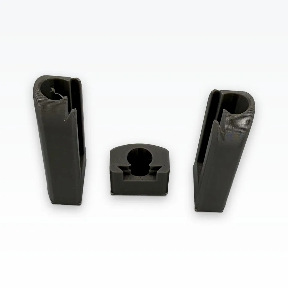 Photo of two grey 3D printed gripper finger bodies standing on their mount faces beside the small mount-fit coupon, seen at an angle