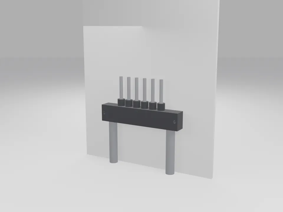 The black manifold screwed to a plain white wall panel, with grey poly lines entering from below and thin tubes rising from the outlets