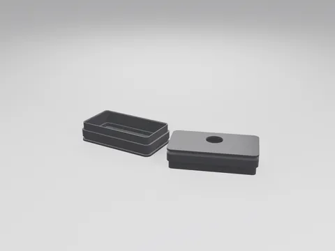 Two black 3D printed rectangular end caps, one turned to show its open side and internal groove, the other with a round port hole